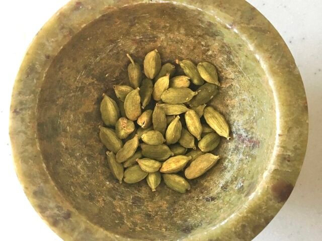 Green cardamom pods in a brass bowl